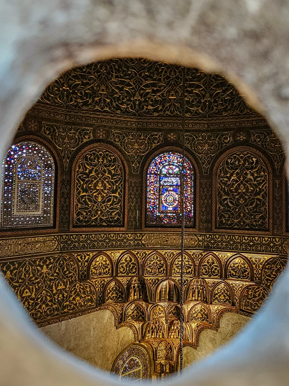 Ornate carved panels and colorful stained-glass windows seen through a circular opening inside a historic building in Cairo