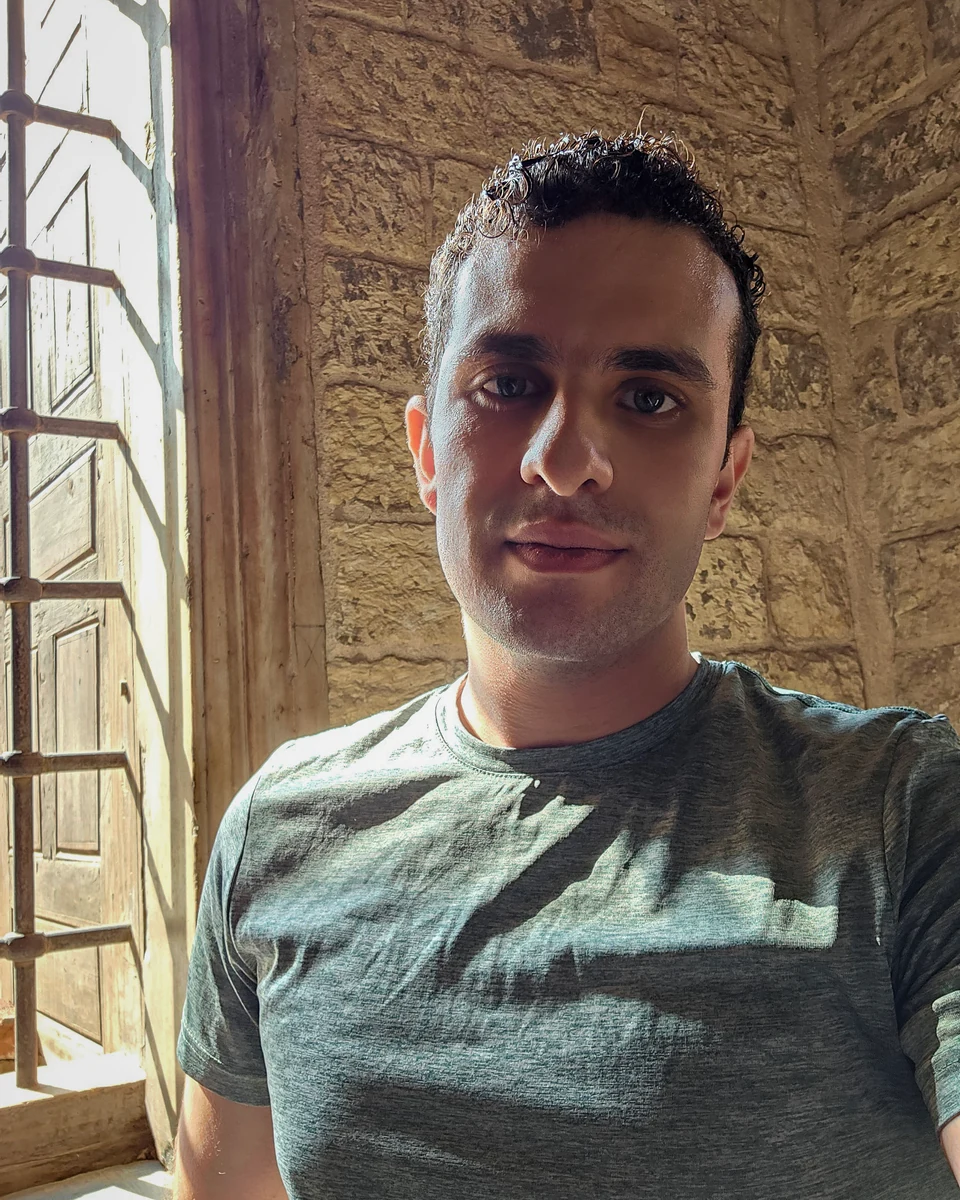 A self-portrait beside a sunlit wooden window and a weathered stone wall