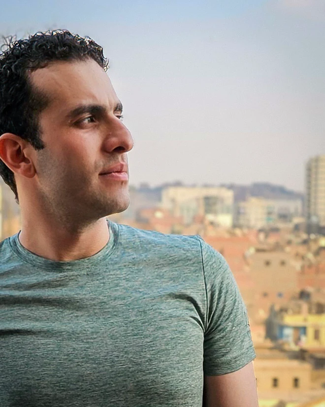 A self-portrait of the author in a teal shirt looking out over Cairo from an elevated window