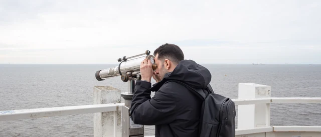 A self-portrait of the author looking through a public telescope across the North Sea, with distant ships on the horizon
